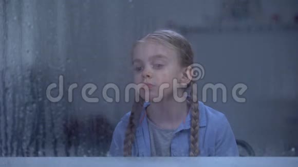 寂寞的女孩在雨天看着窗户等待着父母下班视频的预览图