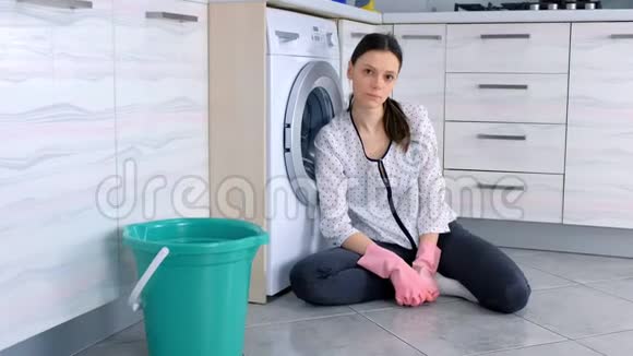 疲惫的女人戴着粉红色的橡胶手套在厨房地板上清洗后看着相机视频的预览图