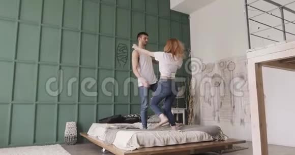 年轻的浪漫夫妇站在床上跳舞微笑和调情关系和爱情观念视频的预览图