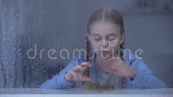 无聊的小女孩在雨天透过窗户看着相机孤独视频的预览图
