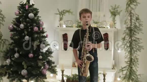 一个英俊的男孩在圣诞树的背景下演奏萨克斯风假日家庭音乐会视频的预览图