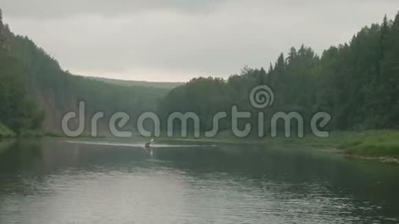 以茂密的松林覆盖着绿色河岸的河景独木舟上的独木舟在河上航行视频的预览图