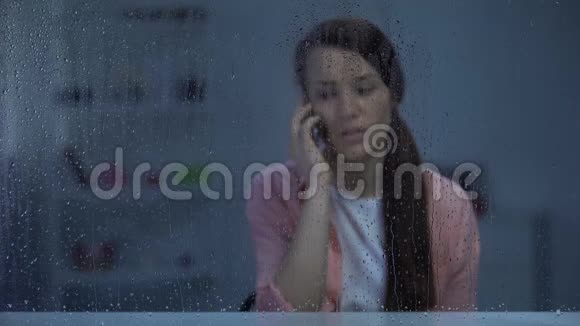 伤心的女人在雨窗后打电话被家人的坏消息震惊视频的预览图
