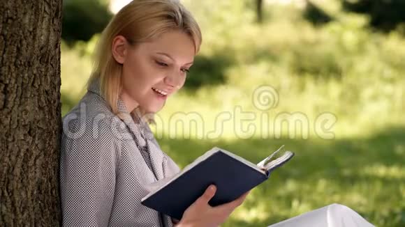 女孩靠在树上在公园里放松坐在草地上自我提升书自我提高和教育观念商务视频的预览图