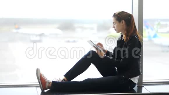 漂亮的女人坐在窗户附近在机场在线查看笔记本电脑上的信息视频的预览图