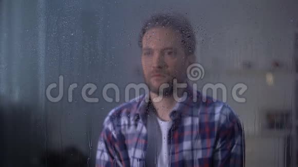 孤独悲伤的中年男子透过雨窗恶劣的天气条件视频的预览图