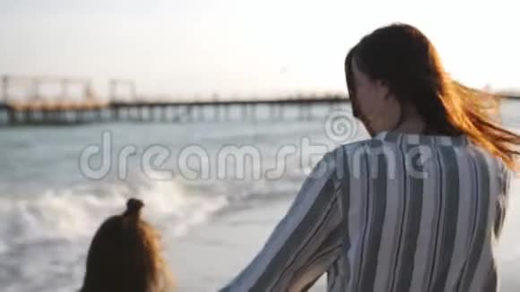 日落时分母亲和小女儿一起在沙滩上散步度假的幸福家庭视频的预览图