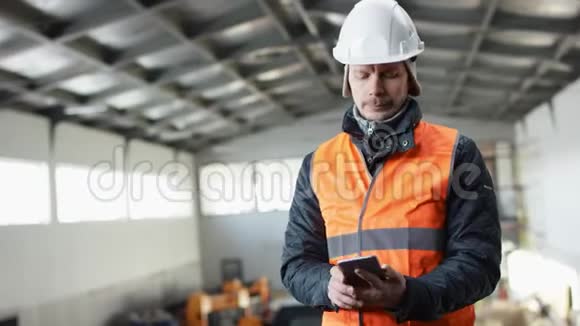 戴着安全帽穿着工作服的胡子和胡子正站在机库的中间用他的电话在视频的预览图