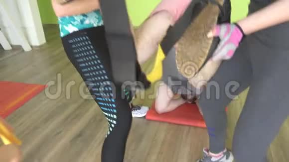 两个漂亮的白种人女孩教练帮助一个胖子在健身房锻炼铰链TRX视频的预览图
