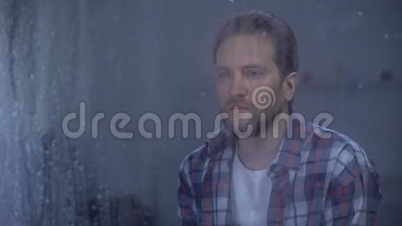 雨天孤独的男人透过窗户看着摄像机抑郁的问题视频的预览图
