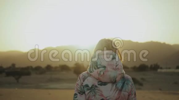 美丽的金发女人在沙漠中日落时散步女性穿越沙漠沙丘特写慢动作4k视频的预览图