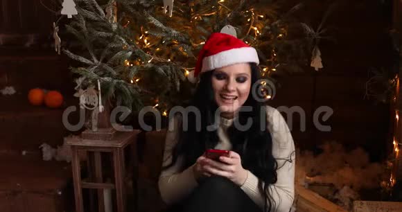 戴着圣诞帽的年轻女孩用手机大笑视频的预览图