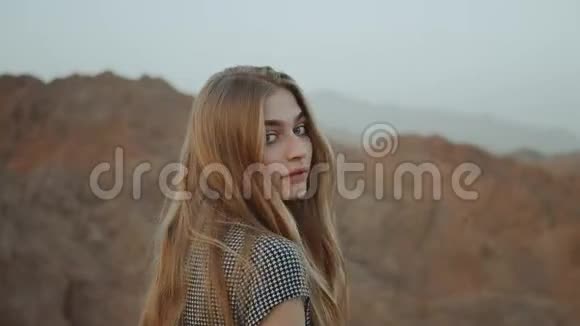 年轻的金发女人穿着长裙走在山顶上带日落的山景慢动作4k视频的预览图