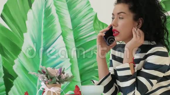 年轻漂亮的女人穿着条纹西装在绿叶的背景下打电话视频的预览图