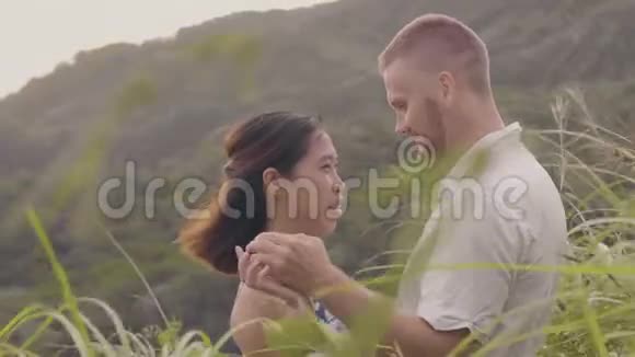 年轻的恋人手牵着手望着热带山景男女握手接吻视频的预览图