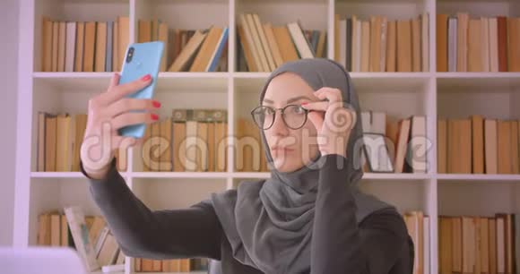 年轻迷人的穆斯林女商人戴着头巾坐在笔记本电脑前打电话自拍的特写视频的预览图