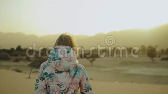 美丽的金发女人在沙漠中日落时散步女性穿越沙漠沙丘特写慢动作4k视频的预览图