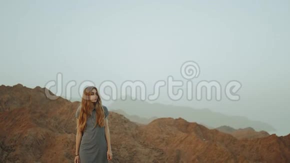 年轻的金发女人穿着长裙走在山顶上带日落的山景慢动作4k视频的预览图
