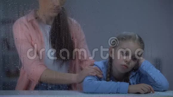母亲在雨窗后扶着小女孩孩子受欺负视频的预览图