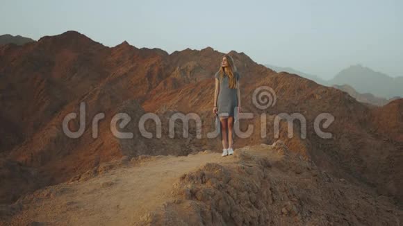站在山顶上的年轻金发女人带日落的山景慢动作4k视频的预览图