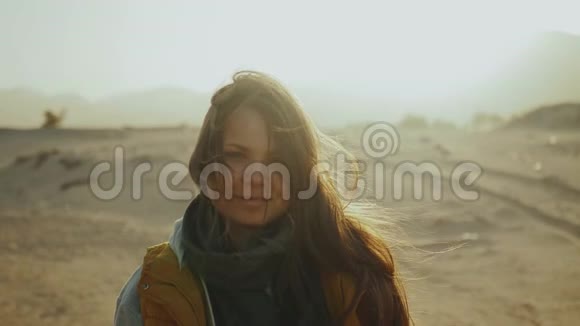 日落时漂亮女人的肖像幸福的年轻女子站在风中对抗沙漠日落景观慢动作视频的预览图