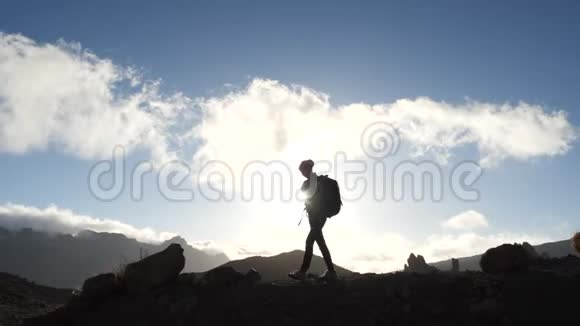 一位年轻女子徒步旅行的剪影背着背包走上山顶迎着蓝天和晚霞视频的预览图