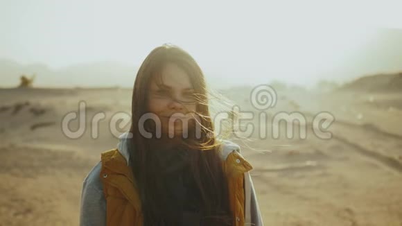 日落时漂亮女人的肖像幸福的年轻女子站在风中对抗沙漠日落景观慢动作视频的预览图