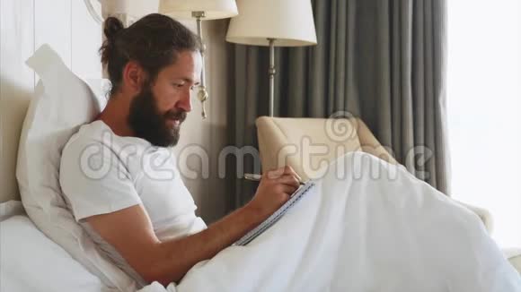 一个大胡子的年轻人在家里的卧室里醒来后在写日记视频的预览图