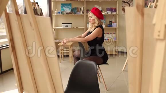 一位年轻的金发女郎在她的工作室里坐在椅子上视频的预览图