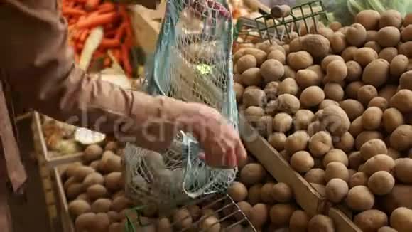 特写女性用手从绿色杂货店的木箱里用一个细绳袋采摘土豆环保包装零废物视频的预览图