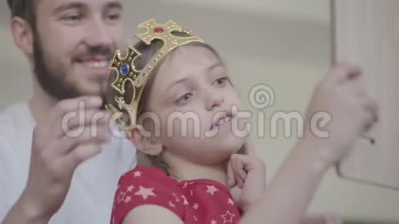 一位漂亮的小胡子父亲把王冠戴在他的小女孩的头上使她成为公主而她的公主视频的预览图