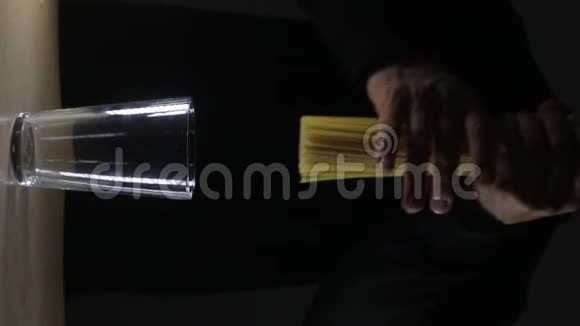 垂直视频男人把金色的生面条放在深黑的背景上视频的预览图