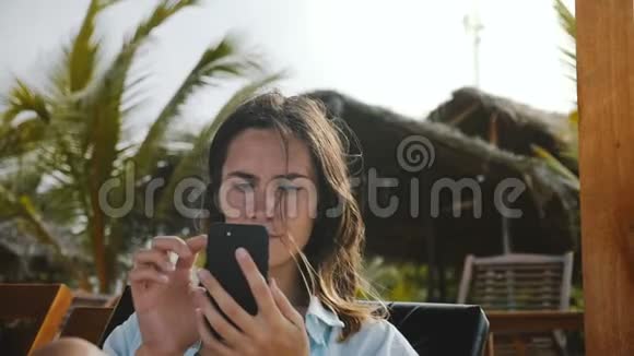快乐自信的女商人坐在海滩躺椅上在度假胜地使用智能手机移动办公应用程序视频的预览图
