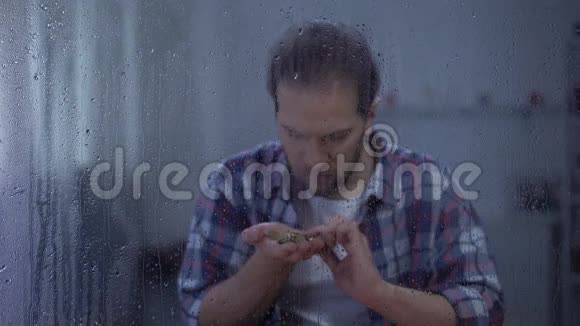 沮丧的人在雨窗后数硬币低收入贫穷的概念视频的预览图