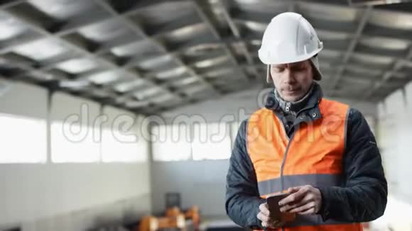 戴着安全帽穿着工作服的胡子和胡子正站在机库的中间用手机拍照视频的预览图