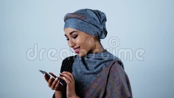 年轻美丽的阿拉伯女人在她的智能手机上在孤立的白色背景下阅读一些感人和可悲的东西视频的预览图