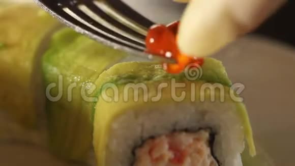 用鳄梨切片装饰的寿司卷的特写用红鱼子酱装饰卷的过程宏观视频的预览图