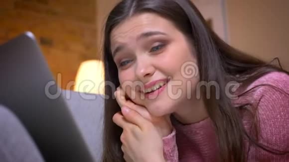 一个年轻漂亮的白种人白种人少女的特写镜头她在笔记本电脑上打了一个视频电话被逗乐了视频的预览图