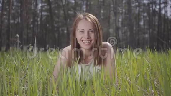 美丽的女人一头棕色的头发绿草中在壮观的森林里笑着视频的预览图