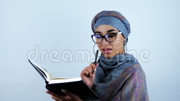 年轻美丽的阿拉伯微笑商务女性在她的策划者在孤立的白色背景上写笔记视频的预览图