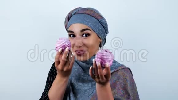 年轻美丽的阿拉伯女人微笑着抱着美味的纸杯蛋糕在孤独的白色背景下玩味着视频的预览图