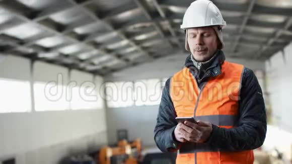 戴着安全帽穿着工作服的胡子和胡子正站在机库的中间并通过他的短信视频的预览图
