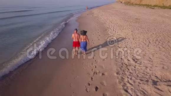 男人和女人在日落时沿着海滩漫步视频的预览图