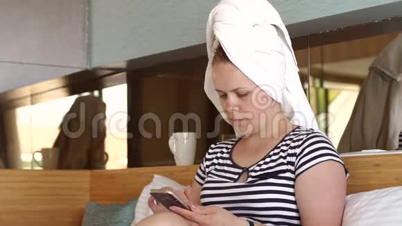 一个头上戴着白色毛巾的女人拿着电话坐在床上视频的预览图