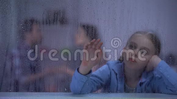 沮丧的女孩坐在雨窗后父母在后台争吵视频的预览图