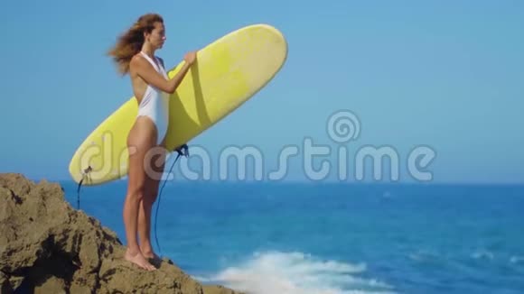 美丽的女人穿着比基尼和冲浪板在海滩上散步性感的冲浪女孩在海滩上健康观念视频的预览图