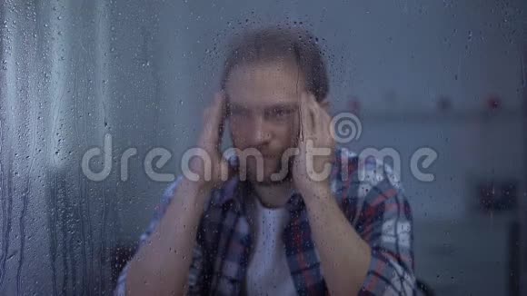 沮丧的男人在雨窗后按摩太阳穴头痛视频的预览图