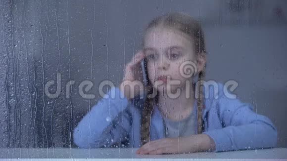 伤心的小女孩在雨天打电话独自呆在家里思念母亲视频的预览图