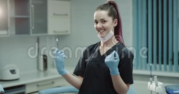 快乐的微笑牙医护士助理准备一个外科注射器注射直看相机和视频的预览图