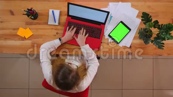 在笔记本电脑上工作的年轻白种人的特写镜头桌上放着绿色屏幕的平板电脑视频的预览图